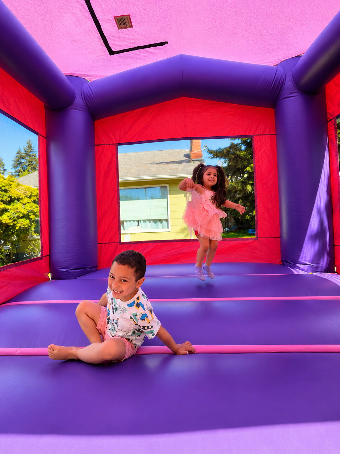 Two kids playing inside a pink and purple bounce house.