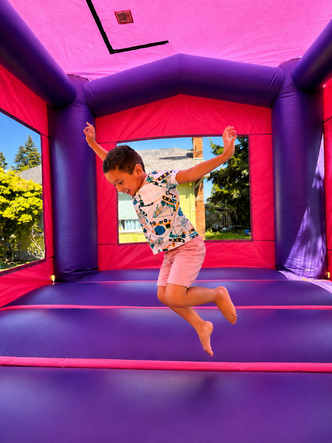 A kid mid-jump inside a pink and purple bounce house in a real Everett backyard.
