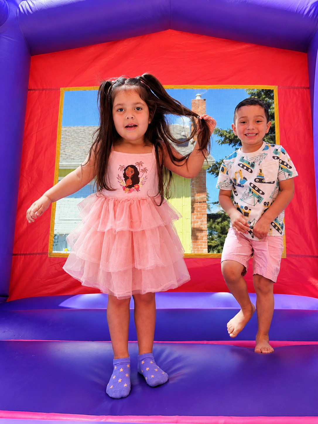 A girl in a pink tutu dress jumping in a red and yellow bounce house.